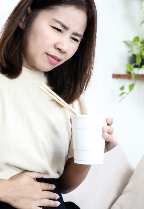 Mujer con malestar estomacal pone su mano en el abdomen y con la otra mano sostiene un vaso de agua probiótica de kéfir