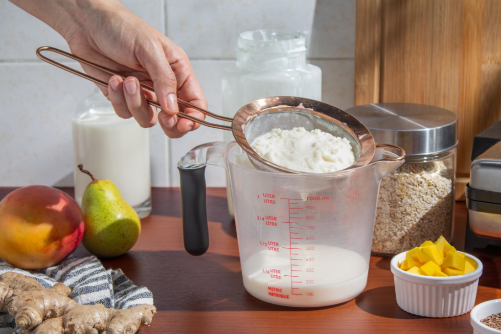 Mano de mujer colando kefir de leche y yogur cayendo en vaso medidor