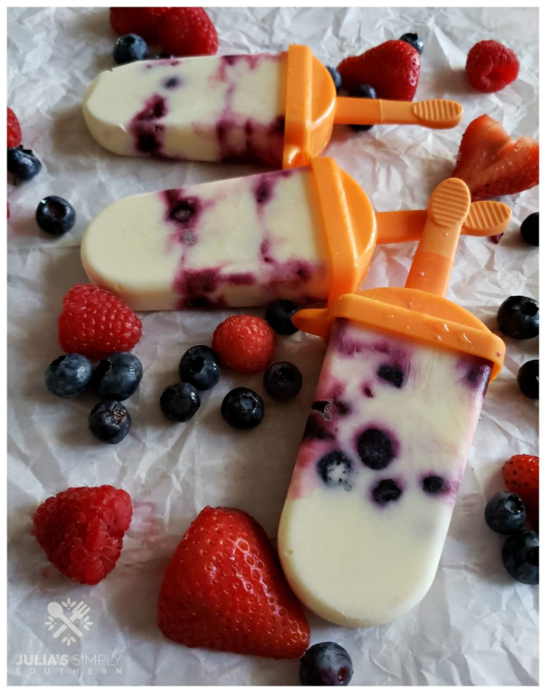 Paletas heladas de frutos rojos en moldes sobre papel y frutos rojos alrededor