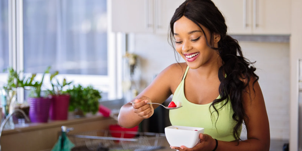 Mujer morena con plato de avena y frutos rojos en la mano comiendo con una cucharilla por ardor de estómago